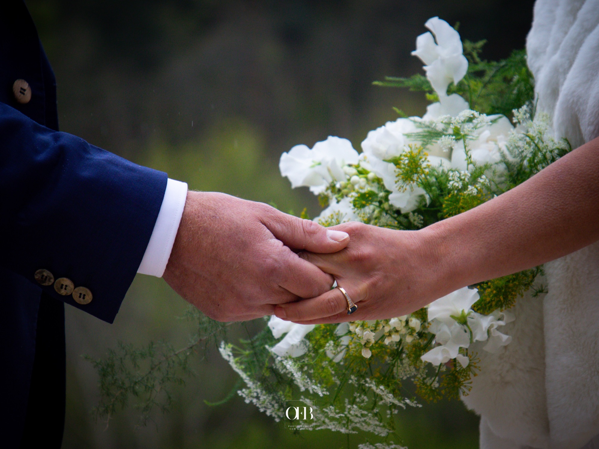 Les mains des mariés et le bouquet de la mariée